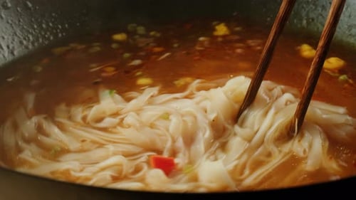 Noodles cooking in hot, spiced broth with chopsticks