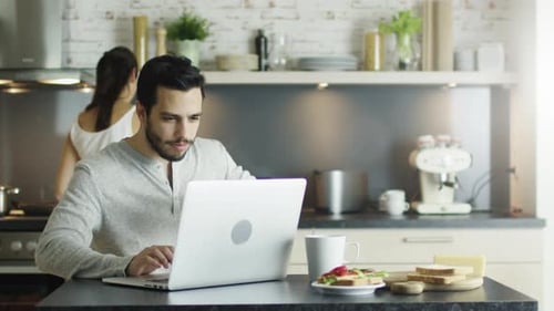 Man Uses Laptop and Drinks Coffee in Kitchen