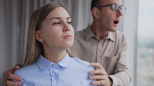 Man Comforting Woman in Office Near Window