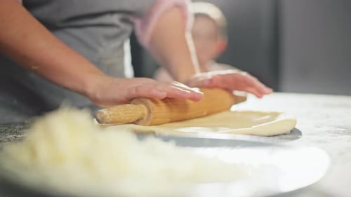 Closeup of Mother's Hands Rolling Out Dough with a Rolling Pin in the Kitchen