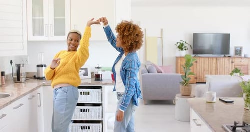 Happy diverse female lesbian couple dancing in kitchen in slow motion