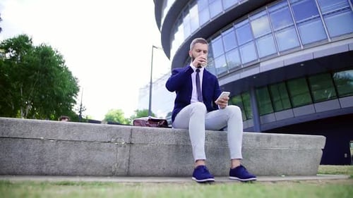 Hipster-Geschäftsmann mit Kaffee und Smartphone sitzt auf einer Bank auf dem