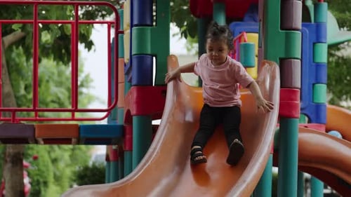 happy toddler baby girl sliding and playing at outdoor playground