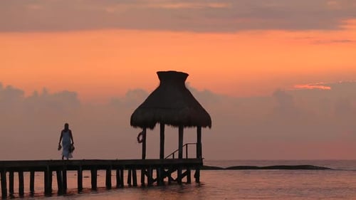 Woman Walks Along Dock During Sunset at Tropical Resort Beach