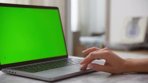 Laptop with Green Screen on Table and Hand Touching Keyboard