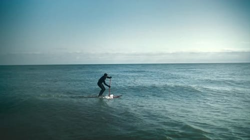 Paddleboarder Gliding on Ocean Waves on Sunny Day