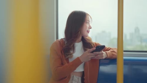 Glückliche junge asiatische Passagierin lächelt und benutzt Smartphone im U-Bahnhof