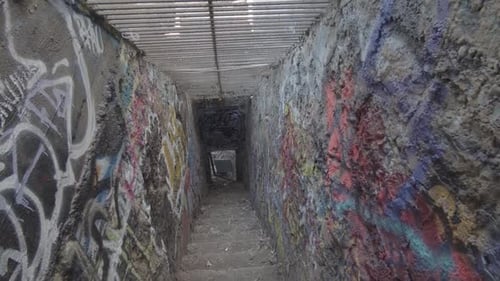 A frightening and dirty corridor leading down the stairs, with graffiti walls and bars on the ceilin