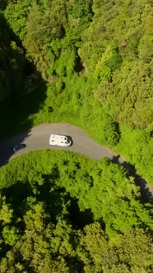 Vertical drone shot around a RV and car on a winding forest road in the mountains