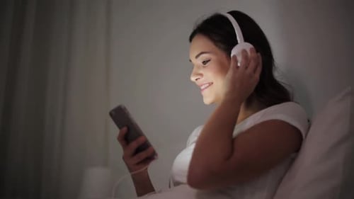 Woman using phone in bed with headphones
