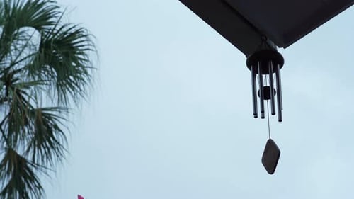 Calming and relaxing view of a wind chime blowing in a tropical garden while it's raining (moody sho