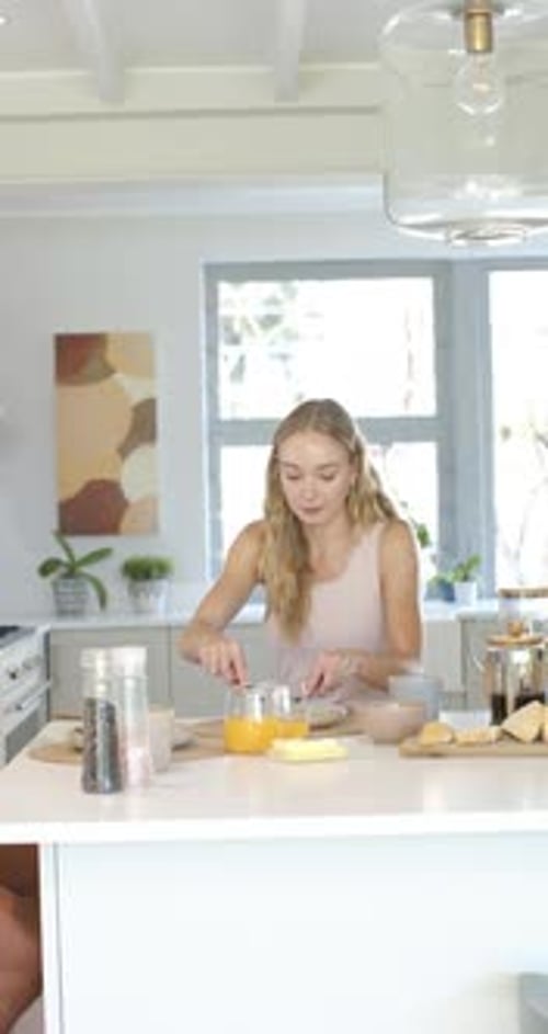 Vidéo verticale : Femme assise sur une île avec OJ préparant le petit déjeuner, étalant et remuant