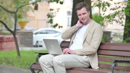 Man With Neck Pain Using Laptop on Park Bench