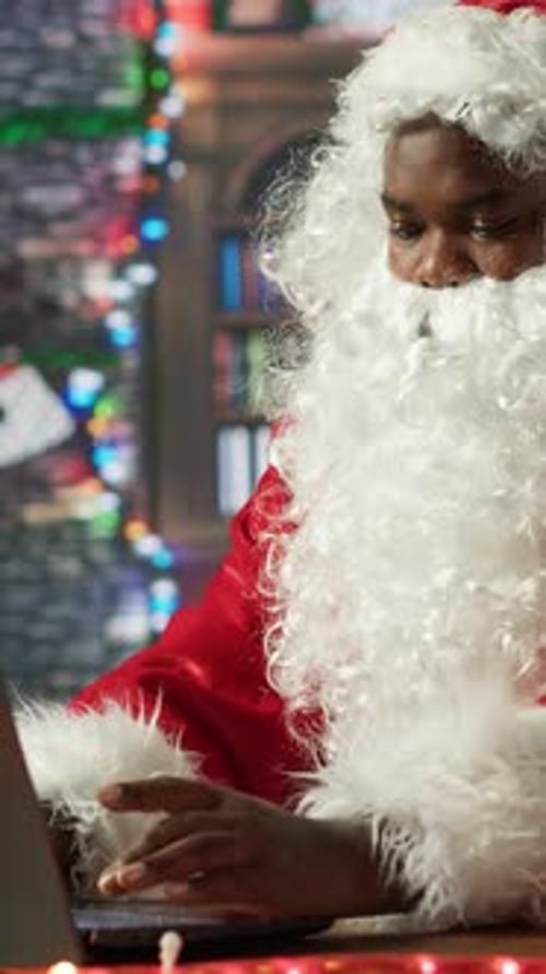 Vertical Video Black Santa Searches Online for Gift Locations Using His Laptop