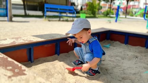 Petit bambin caucasien en barboteuse en jean jouant dans un bac à sable.