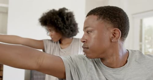 Casal afro-americano espelhando um homem estendendo o braço, se aquecendo em casa, vestindo camisetas cinza
