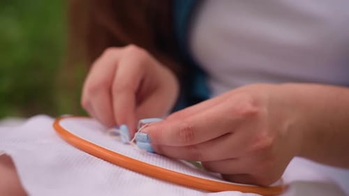 Close Up Of Hands Embroidering Fabric With Needle Outdoors In Natural Light