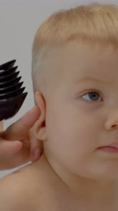 Vídeo vertical: la madre le corta el pelo a un niño pequeño en casa con un cortaúñas y unas tijeras