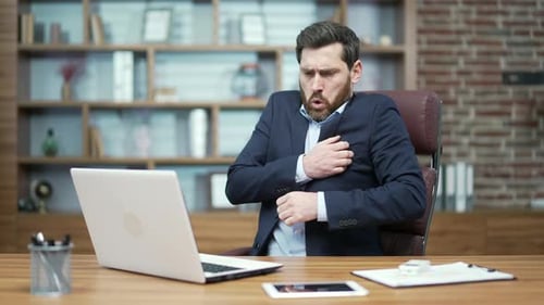 Un homme d'affaires à la barbe froide, un investisseur en costume officiel souffre et tremble, se réchauffe les mains et essaie de travailler