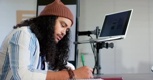 Man picking up pen and writing notebook notes after reviewing laptop charts at desk, copy space