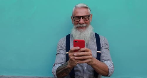 Smiling senior man uses smartphone against teal background