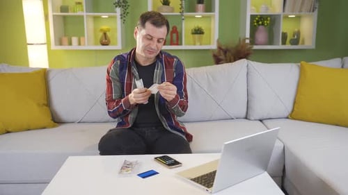 Man Counting Money at Home With Laptop