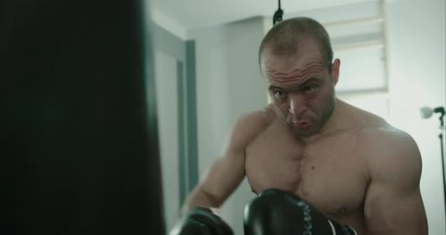 Concentrated man boxer hitting boxing bag in indoor gym with punch combinations