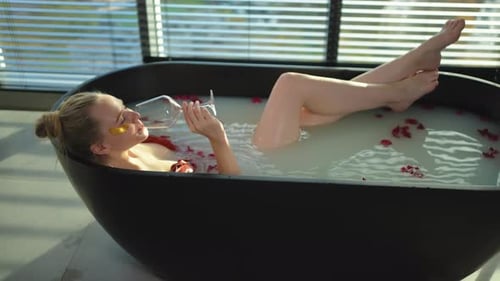 Spa Relaxation Woman Lying in Bath with Holding Glass with Red Wine Girl Relaxing in Bathroom at