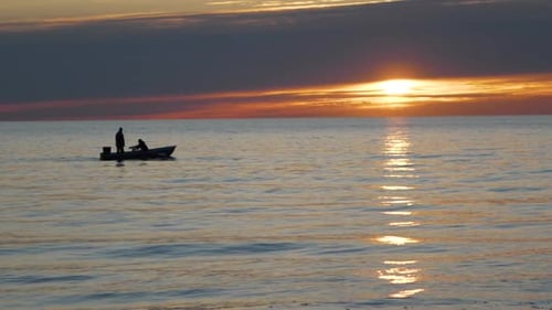 Fishermen in boat sail by sea at sunset