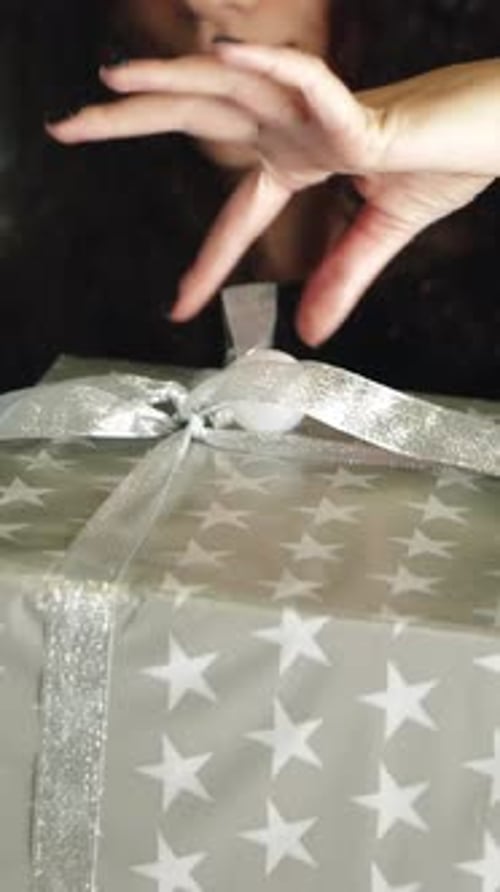 Smiling Woman Opens Birthday Gift with Silver Ribbon