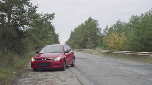 A red car stops on the side of the road due to a malfunction, a flat tire