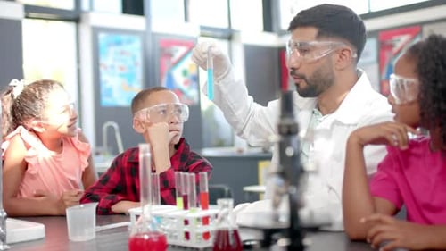 In a school classroom, a biracial teacher demonstrates a chemistry experiment