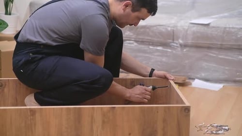 Man Assembles Wooden Cabinet with Power Drill Indoors