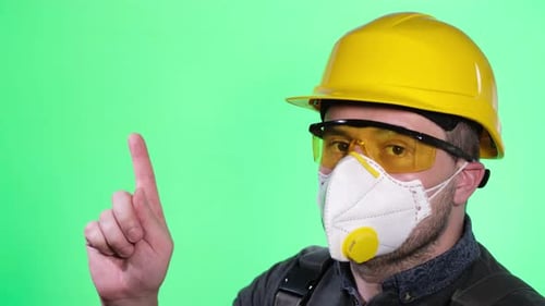 Portrait of a Construction Worker with a Protective Mask Looking at the Camera on a Green Background