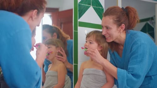 Woman Helps Child Brush Teeth in Bathroom