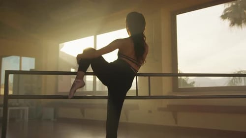 Young Woman Stretching at Ballet Barre in Studio