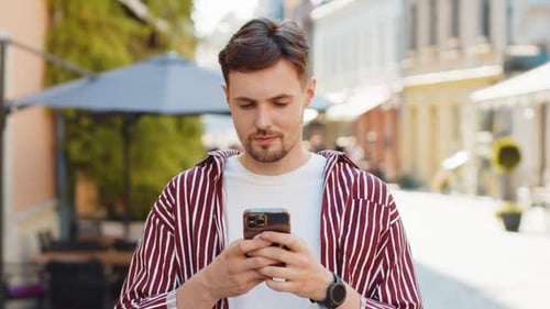 Young Man Using Phone and Smiling in City