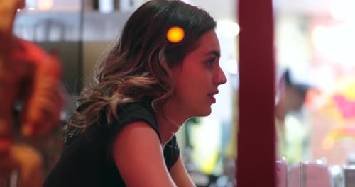 Ehrliche, ungezwungene junge Frau, die nachts im Restaurant durch das Fenster mit einer Person außerhalb der Kamera spricht