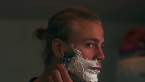 Man with Long Hair Shaves Face in Bathroom