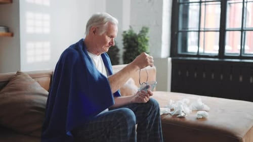 Vieil homme malade respirant à travers un nébuliseur à la maison par inhalation thérapeutique, rétablissement de la santé pulmonaire