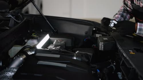 Automechaniker repariert Automotor mit Werkzeugen unter der Arbeitslampe