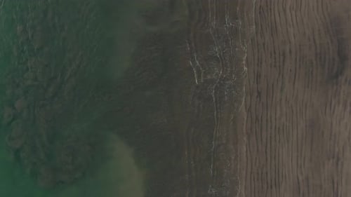 Aerial flight above empty beach with ocean sand swirls in Costa Rica