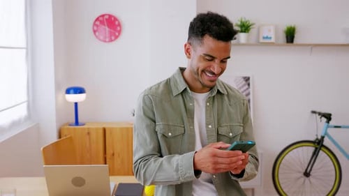 Smiling Young Adult Man Checking Social Media on Smartphone at Home Office