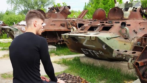Young Man Observing Damaged Military Vehicles Outdoors