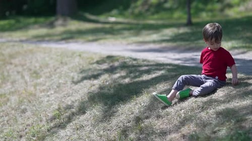 Ein kleiner Junge sitzt auf einer grünen Wiese unter gesprenkeltem Licht und wirft Steine. Kleiner Junge in einem