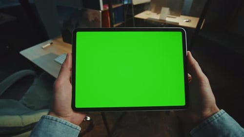 In Dark Office Man Holding Scrolling a Tablet Computer with a Horizontal Green Screen Mockup Display