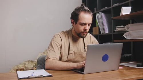 Barista Works on Laptop in Cafe While Preparing for Coffee Roasting and Managing Artisan Coffee