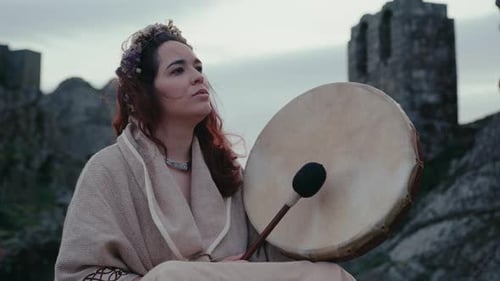 spiritual woman playing a shamanic drum in a beautiful with a old medieval tower behind her