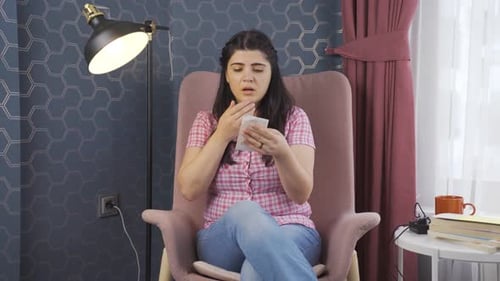 Woman Reading Receipt in Armchair, Looking Concerned