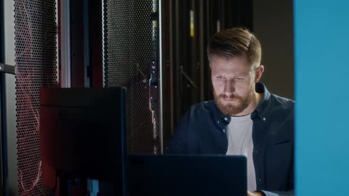 Young Male IT Administrator Working on Laptop in Data Center